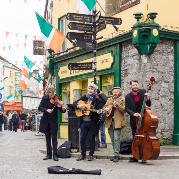 Eine Straßenmusikgruppe spielt in einer mit irischen Flaggen geschmückten Straße in Galway, Irland.