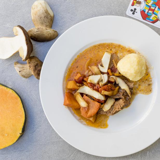 Ein Teller mit Hirschragout, Semmelknödeln, Kürbis und frischen Steinpilzen.