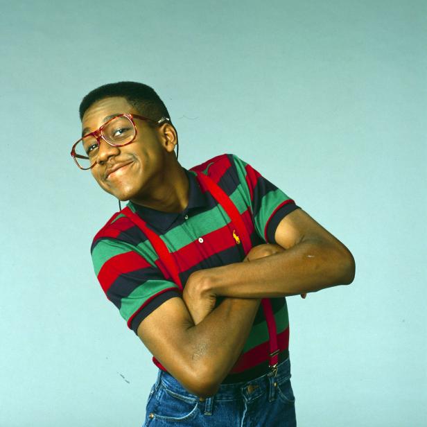 Ein Mann mit Brille, Hosenträgern und gestreiftem Poloshirt lächelt verschmitzt.
