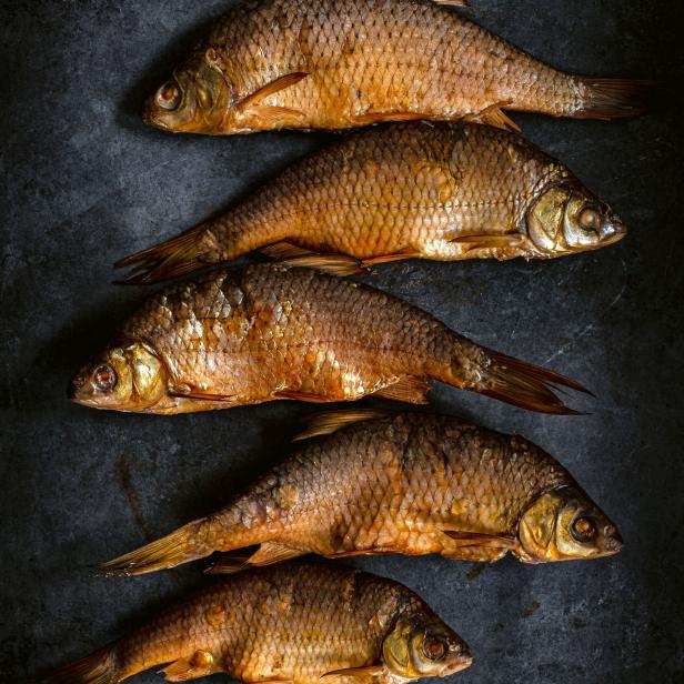 Fünf geräucherte Fische liegen auf einem dunklen Untergrund.