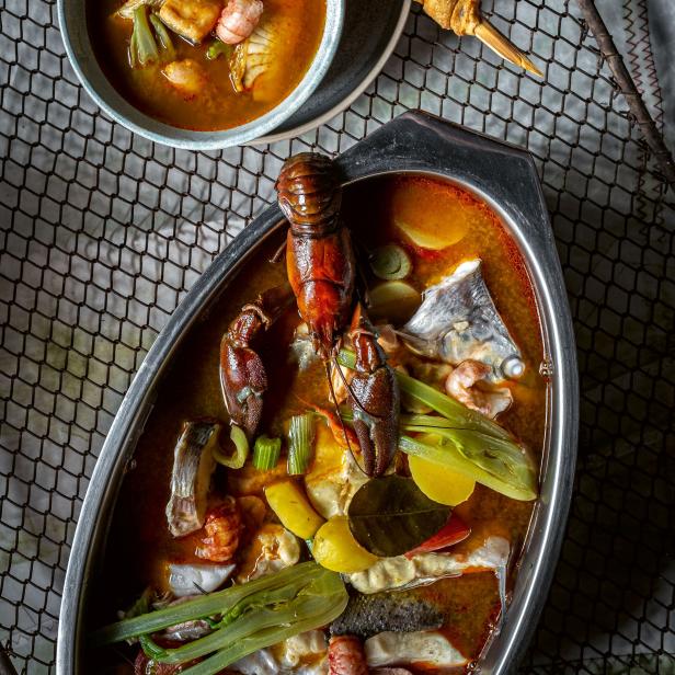 Eine Schale und eine Platte mit Fischsuppe und Langusten, garniert mit Gemüse und Kräutern.