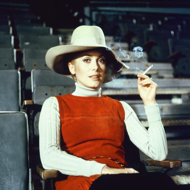 Catherine Deneuve sitzt in einem Theatersaal und raucht eine Zigarette.