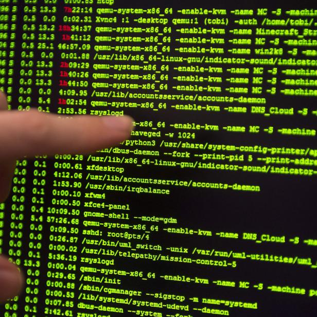 Ein Finger zeigt auf einen Computermonitor mit grünem Code.