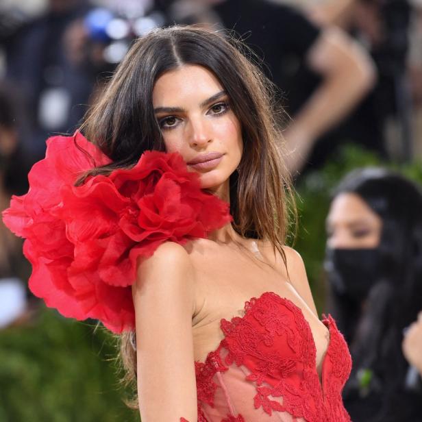 Emily Ratajkowski in einem roten Kleid mit einer großen roten Blume auf der Schulter.