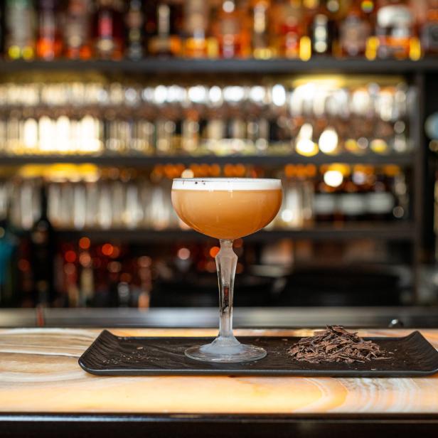 Ein Cocktail mit Schaumhaube steht auf einem Tablett mit Schokoladenraspeln an einer Bar.