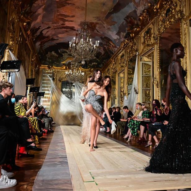 Eine Modenschau in einem prunkvollen Saal mit Models und Zuschauern.