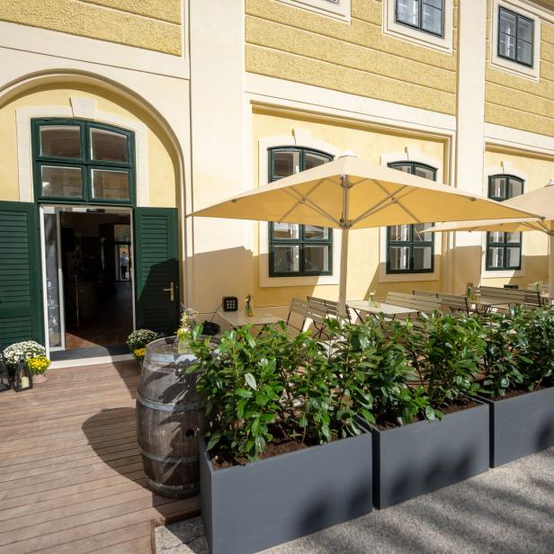 Einladender Außenbereich eines Restaurants mit Tischen unter Sonnenschirmen und dekorativen Pflanzenkübeln.