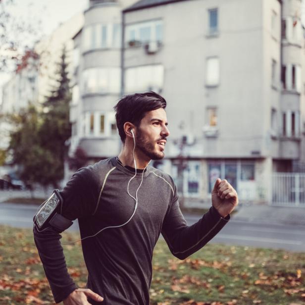 Ein Mann joggt mit Kopfhörern und einem Smartphone-Armband durch eine städtische Umgebung.