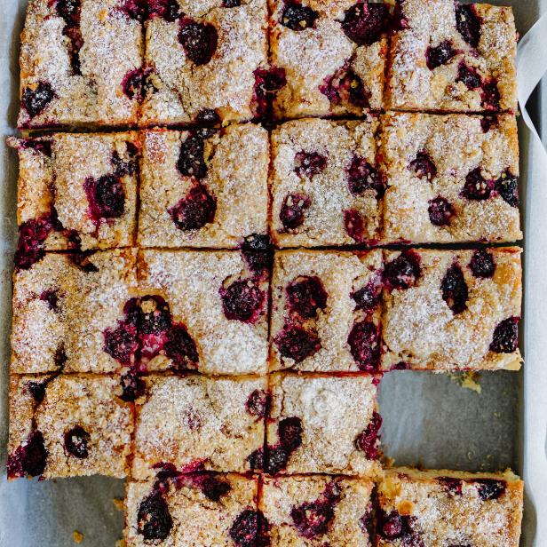 Ein Backblech mit Brombeerkuchen, der in Quadrate geschnitten und mit Puderzucker bestreut ist.