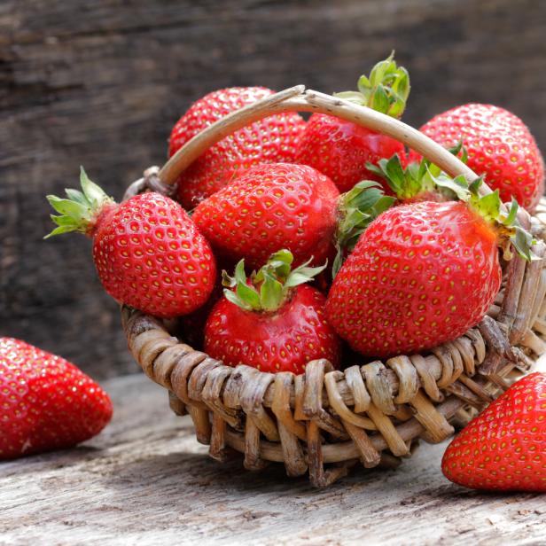Ein Korb voller reifer, roter Erdbeeren auf einem Holztisch.