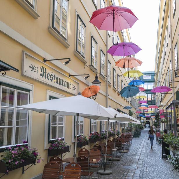 Eine Gasse mit einem Restaurant und bunten, schwebenden Regenschirmen.