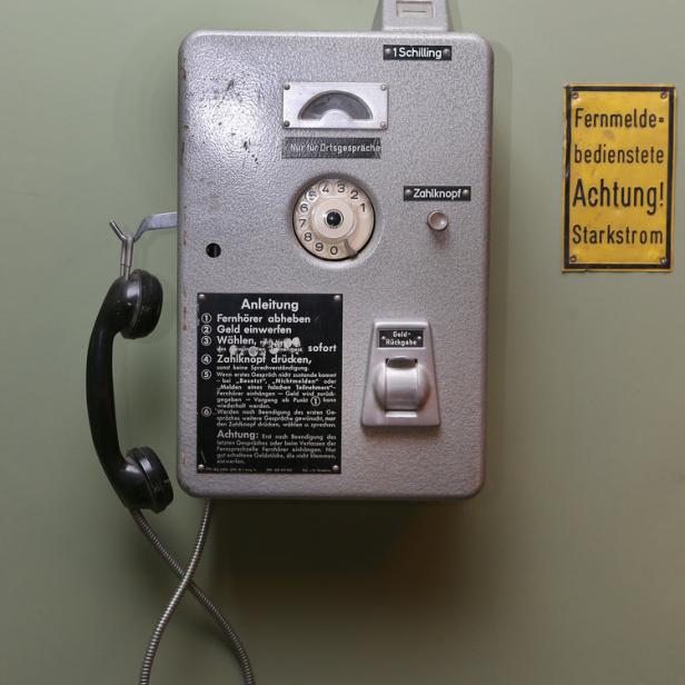 Eine alte, öffentliche Telefonzelle mit Wählscheibe und Bedienungsanleitung an einer Wand.
