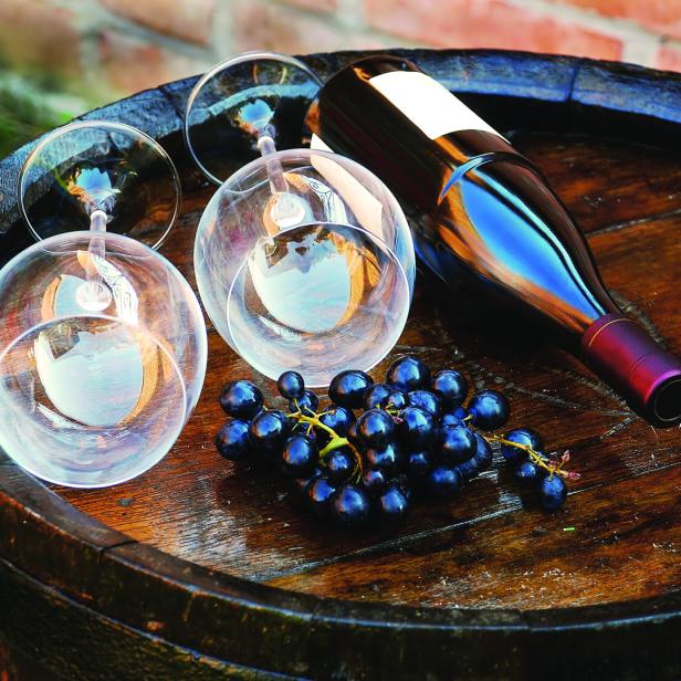 Eine Flasche Wein, Trauben und Weingläser liegen auf einem Holzfass.