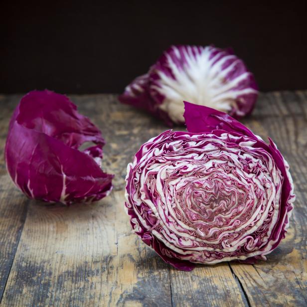 Drei Köpfe Radicchio Salat liegen auf einem Holztisch.