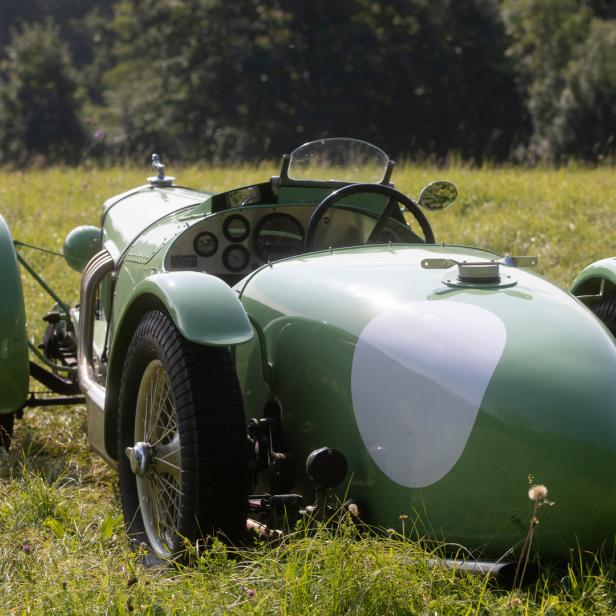 Ein grüner Oldtimer mit weißem Streifen steht im Gras.