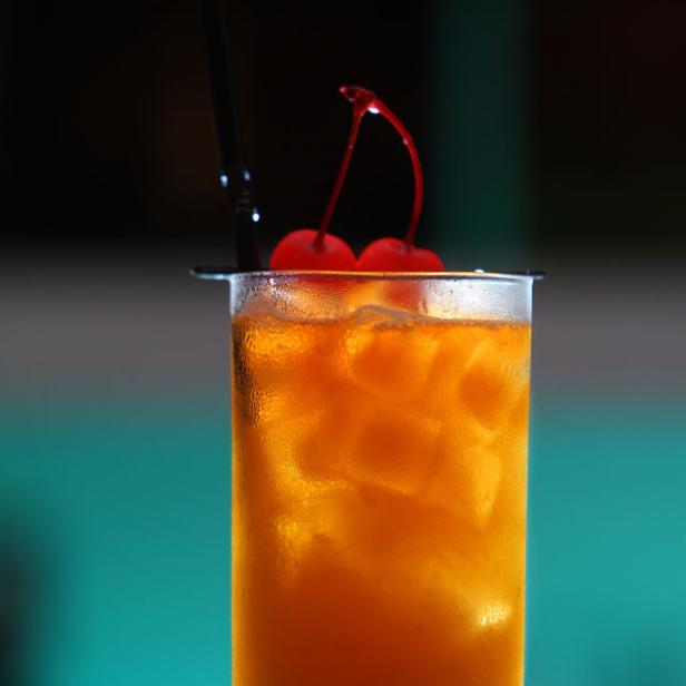 Ein Longdrink mit Eis und Kirschen wird mit einem Strohhalm serviert.