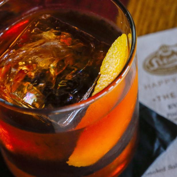 Ein Old Fashioned Cocktail mit einem großen Eiswürfel und einer Orangenzeste.