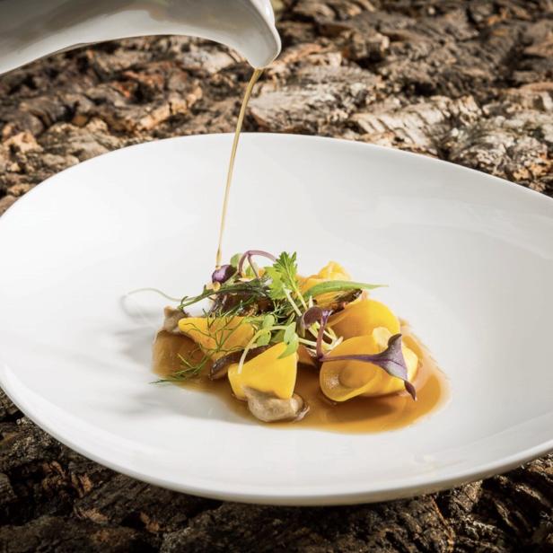 Eine Person gießt Soße über ein Gericht mit Tortellini und Kräutern.