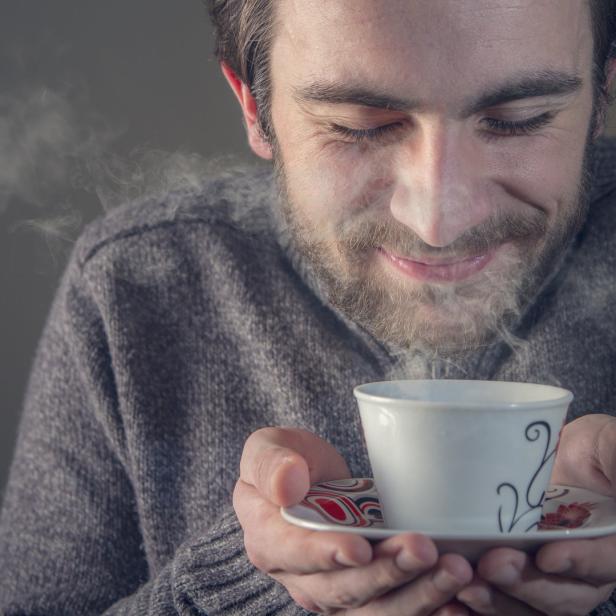 Ein Mann mit Bart hält eine Tasse mit heißem Getränk in seinen Händen.