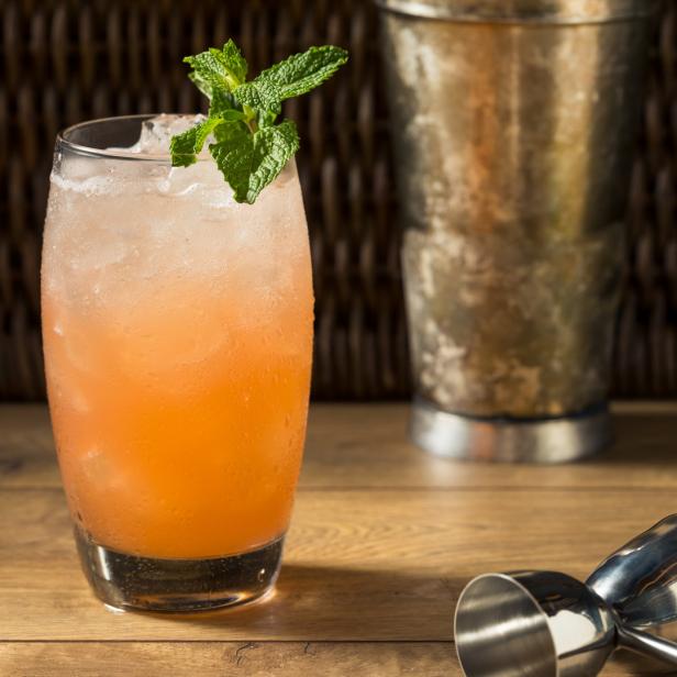 Ein erfrischender, orangefarbener Cocktail mit Minze und Eiswürfeln auf einem Holztisch.