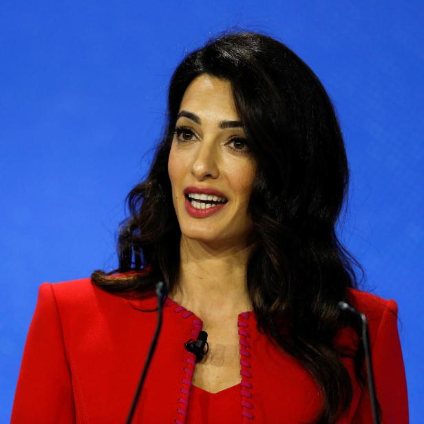 Amal Clooney in einem roten Blazer vor einem blauen Hintergrund.