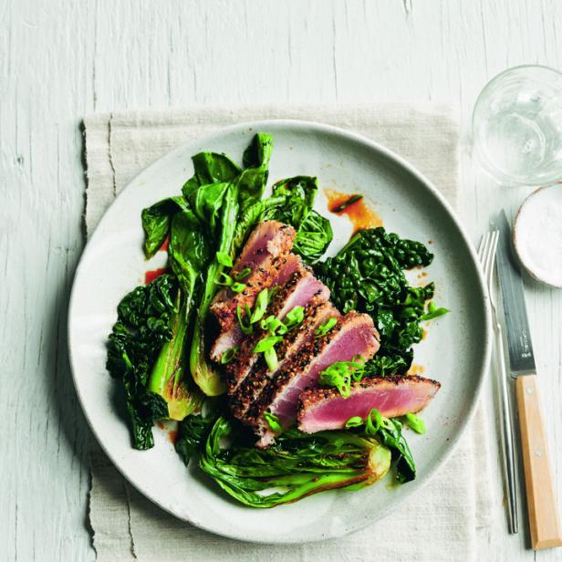 Ein Teller mit angebratenem Thunfisch, serviert auf Pak Choi und Grünkohl, garniert mit Frühlingszwiebeln.