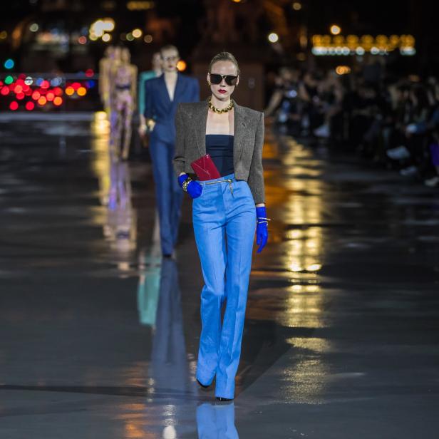 Eine Frau in blauen Hosen und einer Jacke läuft über einen Laufsteg.