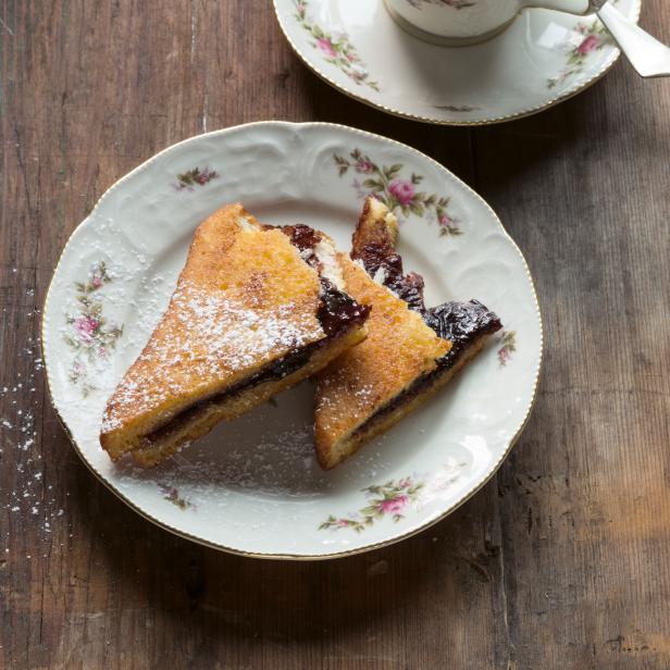Ein Teller mit Marmeladentoast und eine Tasse Kaffee mit Sahne auf einem Holztisch.