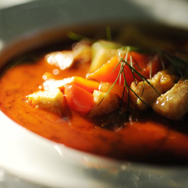 Eine Schüssel mit Tomatensuppe, Croutons und Dill garniert.