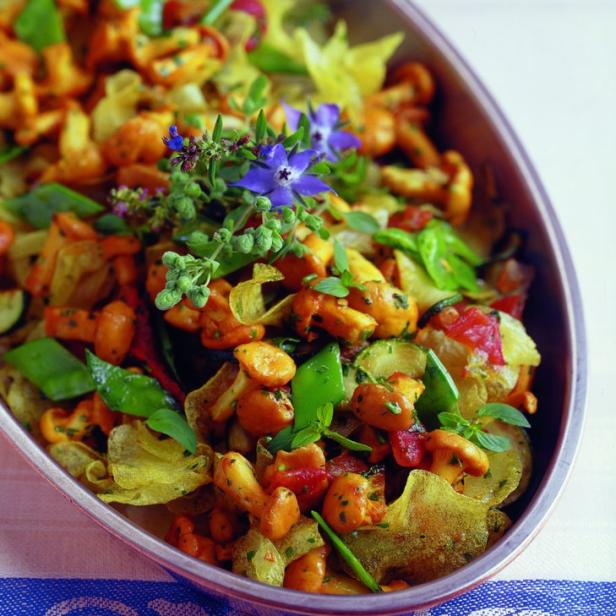 Eine Schüssel mit gebratenen Pfifferlingen, Kartoffelchips und Gemüse, garniert mit blauen Blüten.