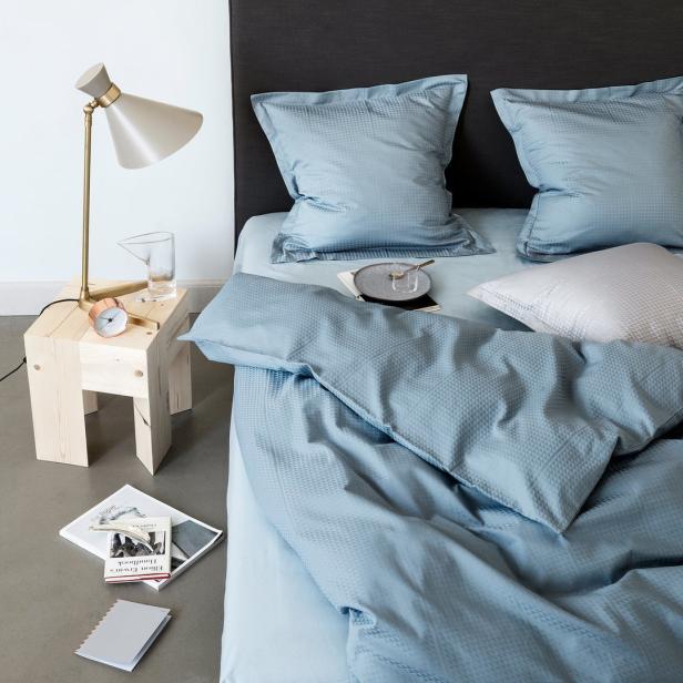 Ein Bett mit hellblauer Bettwäsche, einem Nachttisch und einer Lampe.