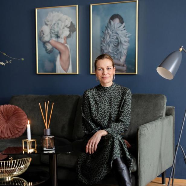 Eine Frau sitzt auf einem Sofa in einem Wohnzimmer mit dunklen Wänden und zwei gerahmten Bildern.