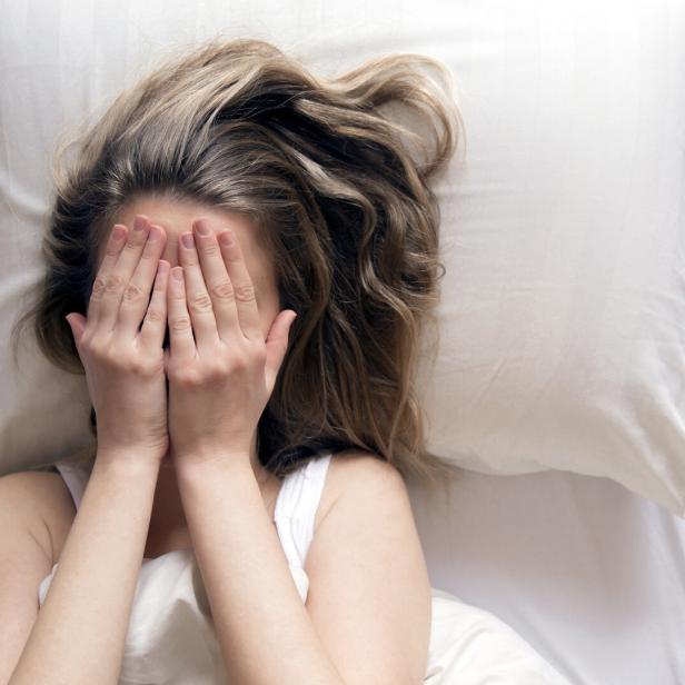 Sie bedeckt im Bett ihr Gesicht mit ihren Händen.