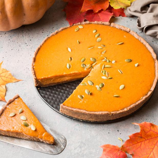 Ein Kürbiskuchen mit Kürbiskernen und Herbstlaub liegt auf einem Tisch.