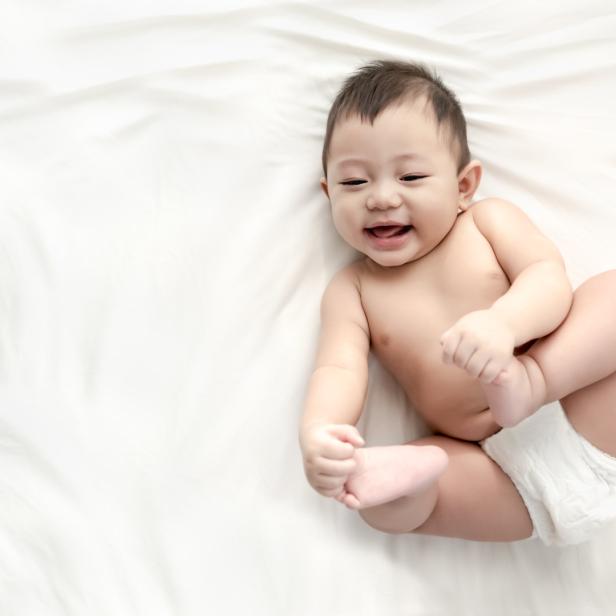 Ein lächelndes Baby liegt auf dem Rücken auf einem weißen Tuch.