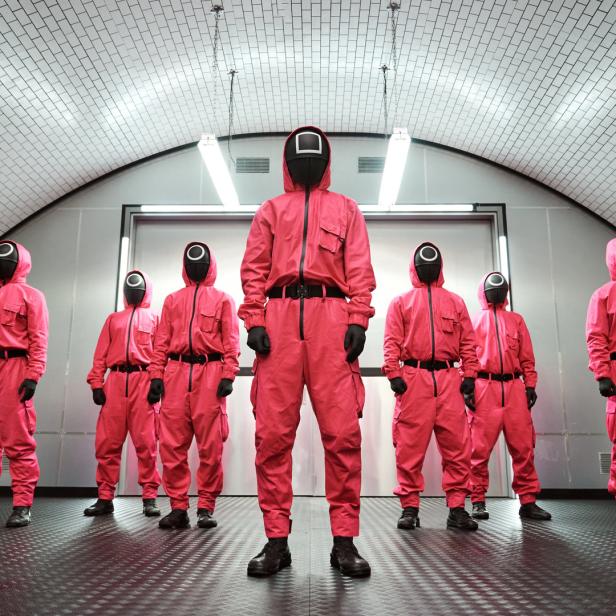 Eine Gruppe von Personen in pinkfarbenen Overalls und Masken, die an die Serie „Squid Game“ erinnern.