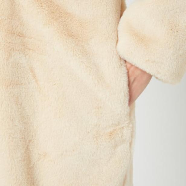 Nahaufnahme einer Hand in der Tasche eines beigen Teddyfleece-Mantels.