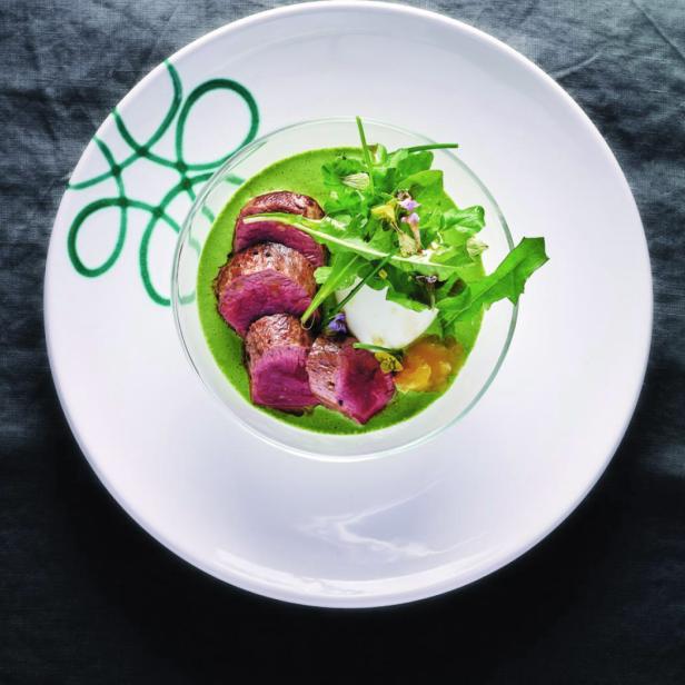 Ein Teller mit rosa gebratenem Fleisch, grüner Soße, Salat und einem pochierten Ei.