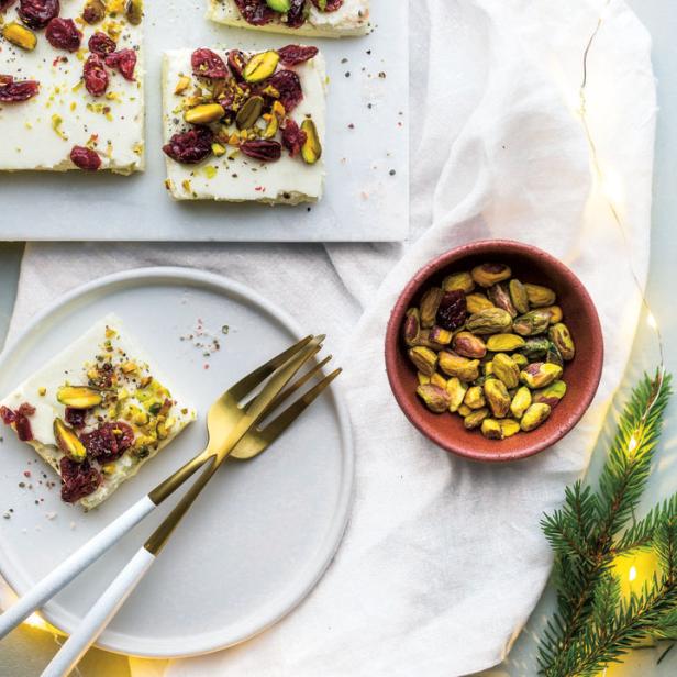 Quadrate aus weißem Fudge, garniert mit Pistazien und Cranberries, auf einem Tisch präsentiert.