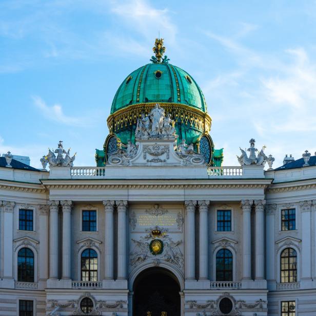 Die Hofburg in Wien mit ihrer markanten grünen Kuppel unter blauem Himmel.