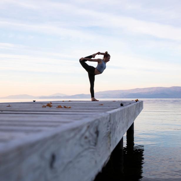 Eine Frau macht Yoga auf einem Holzsteg am See.