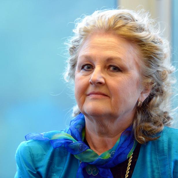 Eine Frau mit blond gelocktem Haar und einem blauen Schal blickt in die Kamera.
