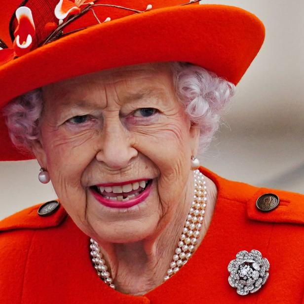 Königin Elisabeth II. lächelt in einem orangefarbenen Hut und Mantel.