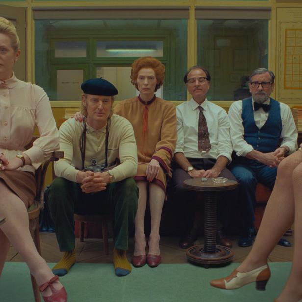 Eine Gruppe von Personen, darunter Tilda Swinton und Owen Wilson, sitzt in einem Wartezimmer.