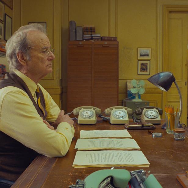 Bill Murray sitzt an einem Schreibtisch mit Telefonen und Dokumenten.