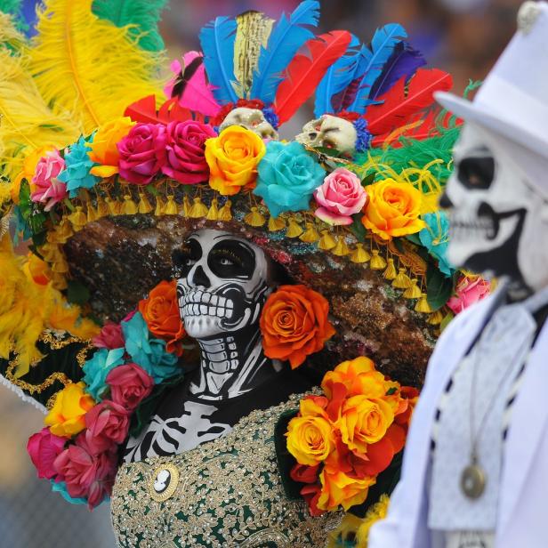Personen mit Gesichtsbemalung und farbenfrohen Kostümen feiern den „Dia de los Muertos“.