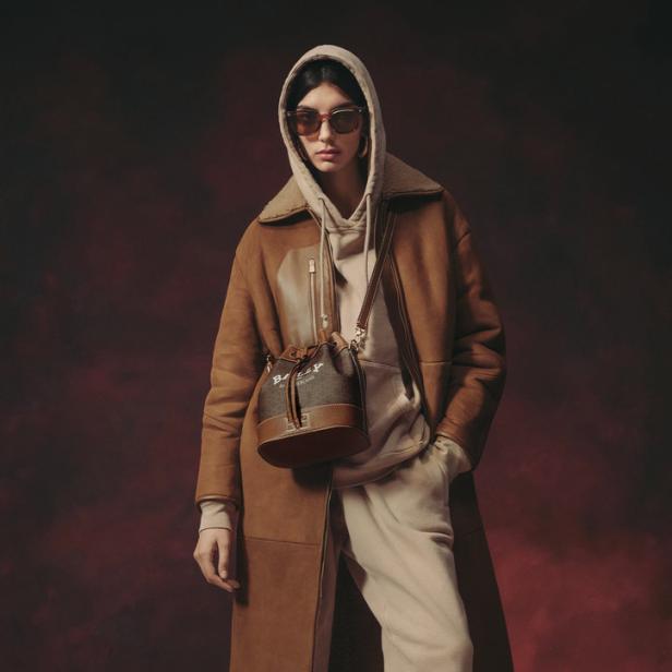 Eine Frau mit Sonnenbrille, Kapuzenpullover, Shearling-Mantel und einer Bally-Handtasche.