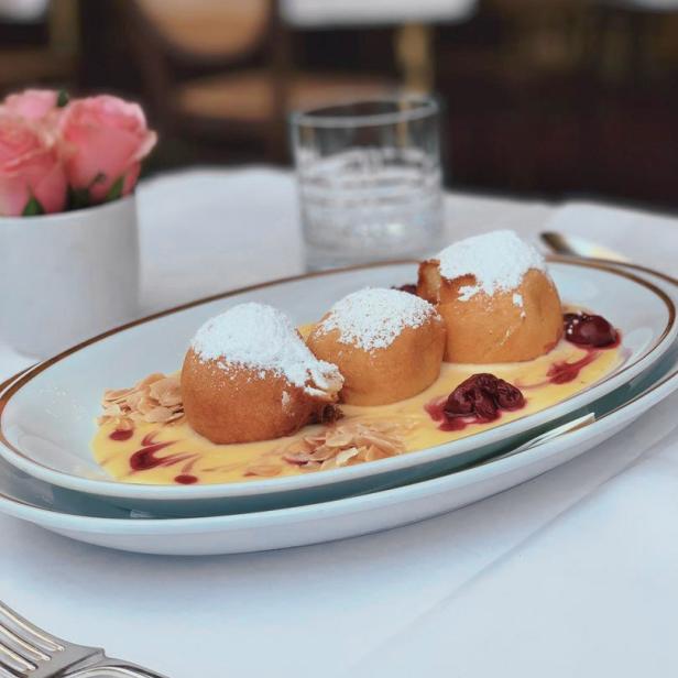 Drei Germknödel mit Puderzucker, Mandeln und Vanillesauce auf einem Teller.