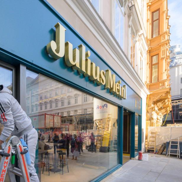 Ein Mann putzt die Fenster des Geschäfts „Julius Meinl“.