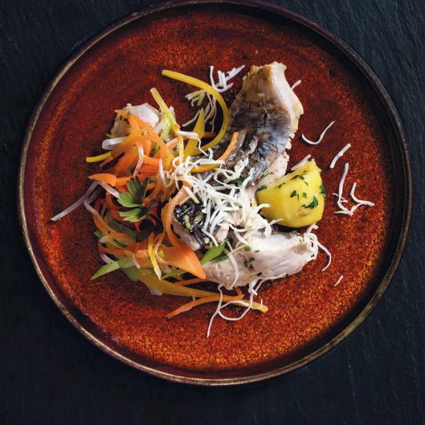 Ein Teller mit Fisch, Kartoffeln und Julienne-Gemüse auf einem dunklen Untergrund.